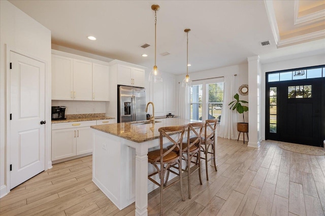 kitchen featuring light wood-type flooring, an island with sink, light stone counters, white cabinetry, and stainless steel fridge