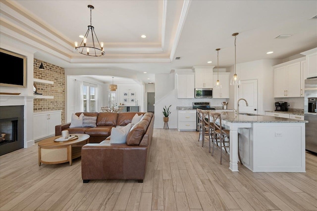 living area featuring light wood-style flooring, an inviting chandelier, a tray ceiling, and ornamental molding