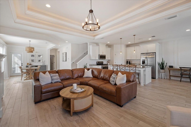 living room with a raised ceiling, an inviting chandelier, and light wood-style flooring