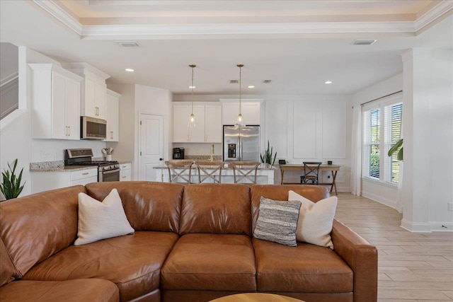 living area featuring visible vents, light wood-style flooring, and ornamental molding