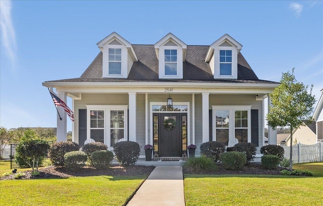 cape cod house featuring a front yard, fence, covered porch, and a shingled roof