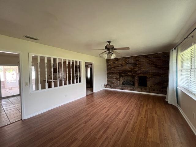 unfurnished living room featuring a brick fireplace, ceiling fan, and dark hardwood / wood-style flooring