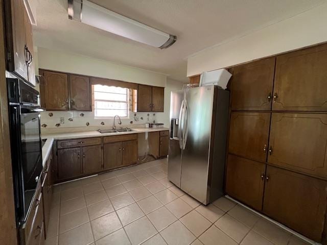 kitchen featuring tasteful backsplash, light tile patterned flooring, stainless steel fridge, black double oven, and sink