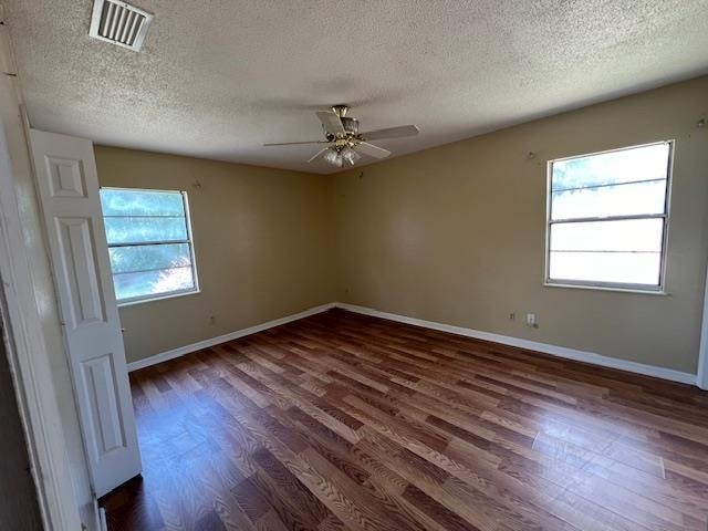 empty room featuring ceiling fan, plenty of natural light, a textured ceiling, and dark hardwood / wood-style flooring