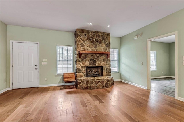 living room with baseboards, hardwood / wood-style flooring, and a stone fireplace