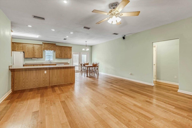 kitchen with brown cabinets, visible vents, freestanding refrigerator, light wood finished floors, and a peninsula