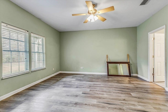 unfurnished room with a ceiling fan, visible vents, wood finished floors, and baseboards