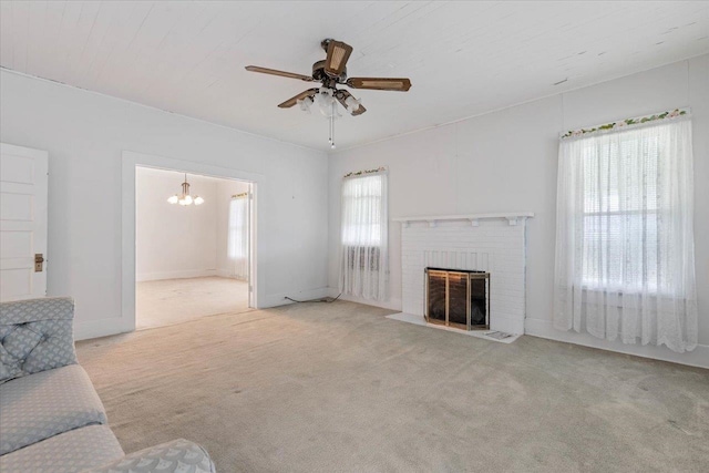 unfurnished living room with ceiling fan with notable chandelier, light colored carpet, and a brick fireplace