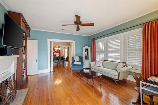 living room with crown molding, ceiling fan with notable chandelier, light hardwood / wood-style floors, and a brick fireplace