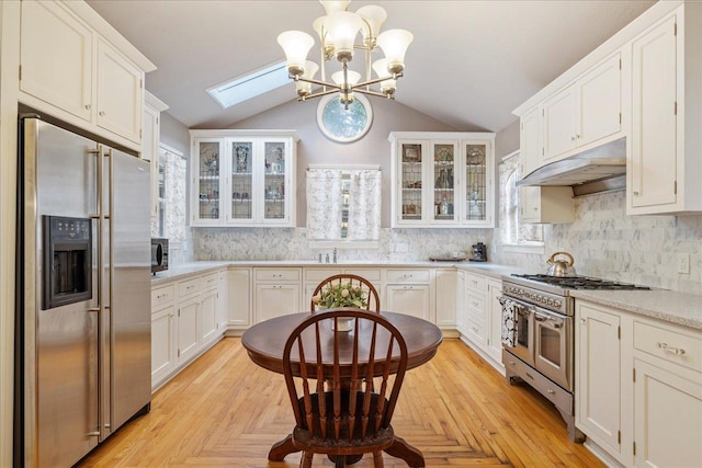 kitchen with hanging light fixtures, stainless steel appliances, vaulted ceiling with skylight, tasteful backsplash, and white cabinets