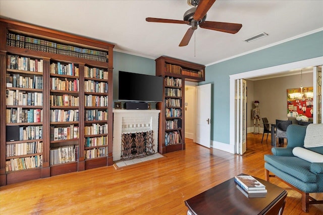 living room with ceiling fan with notable chandelier, ornamental molding, a fireplace, and hardwood / wood-style floors