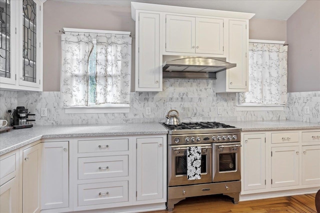 kitchen with white cabinets, plenty of natural light, range with two ovens, and exhaust hood