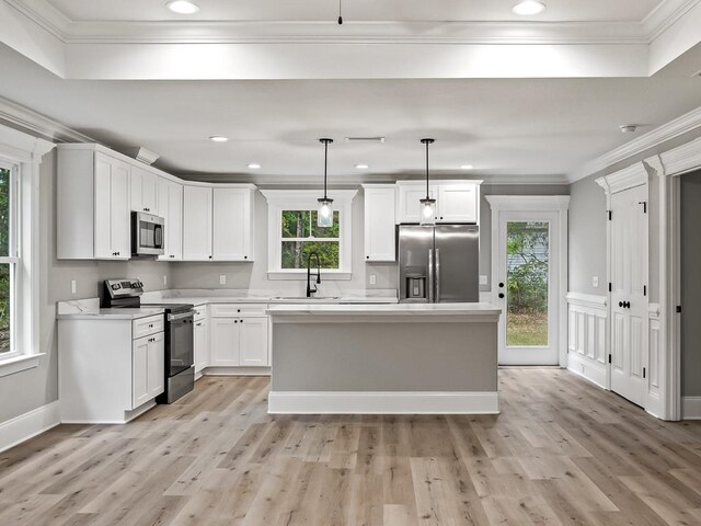 kitchen with hanging light fixtures, white cabinets, stainless steel appliances, and light hardwood / wood-style floors