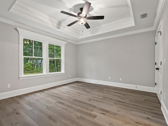 empty room featuring hardwood / wood-style floors, ceiling fan, ornamental molding, and a tray ceiling