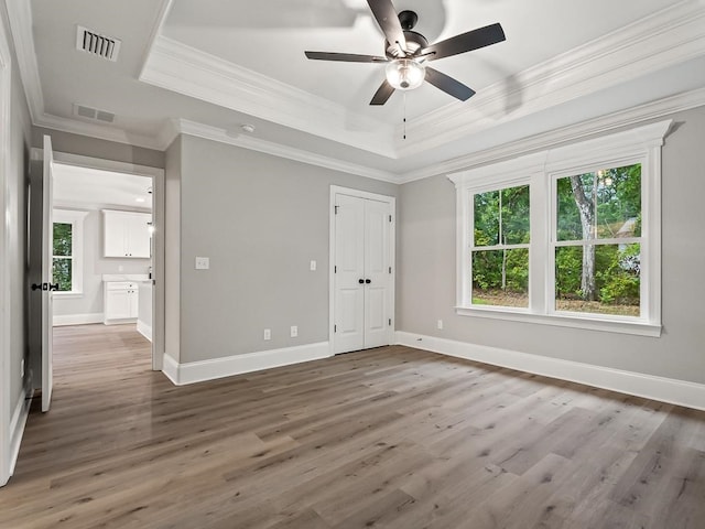 unfurnished bedroom with dark wood-type flooring, crown molding, ceiling fan, a tray ceiling, and a closet