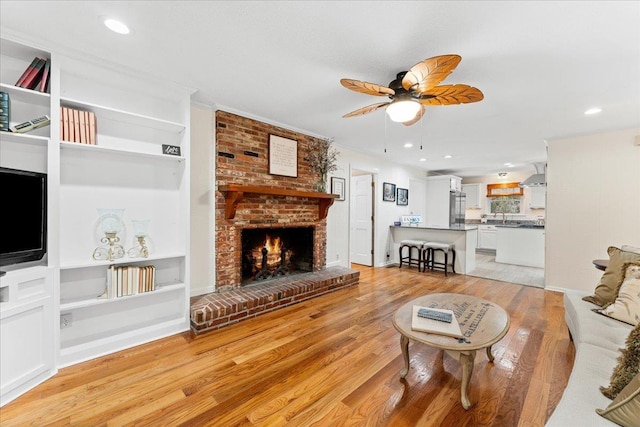 living room featuring ceiling fan, sink, crown molding, light hardwood / wood-style floors, and a fireplace