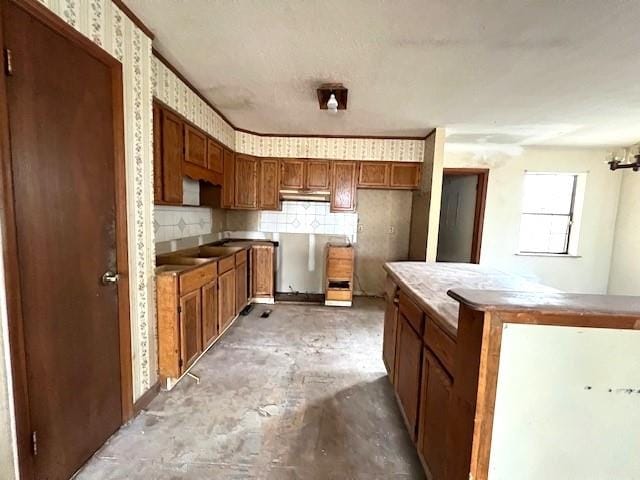 kitchen with brown cabinets, concrete floors, decorative backsplash, and wallpapered walls