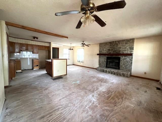 unfurnished living room featuring ceiling fan, a stone fireplace, and baseboards