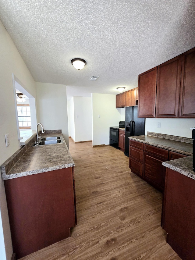kitchen featuring visible vents, dark wood-type flooring, black fridge, a textured ceiling, and a sink