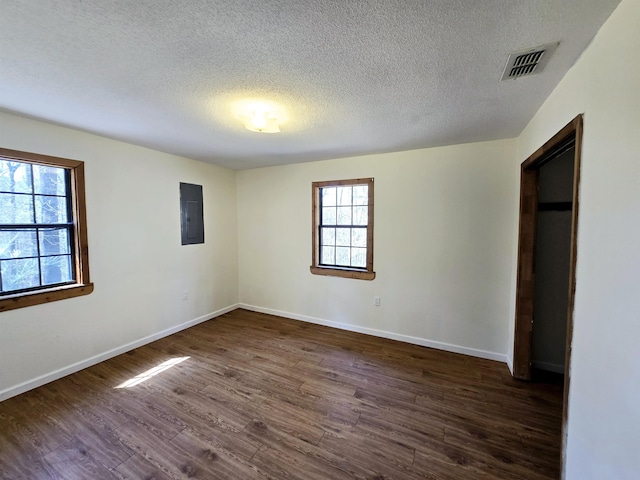 unfurnished bedroom featuring visible vents, electric panel, a textured ceiling, baseboards, and dark wood-style flooring