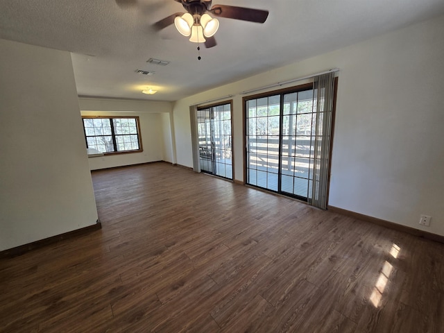 empty room with ceiling fan, visible vents, baseboards, and dark wood finished floors