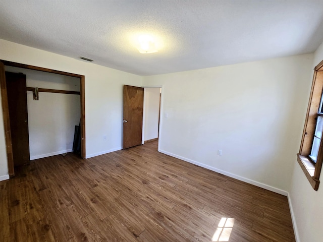 unfurnished bedroom with visible vents, a textured ceiling, baseboards, and dark wood-style flooring