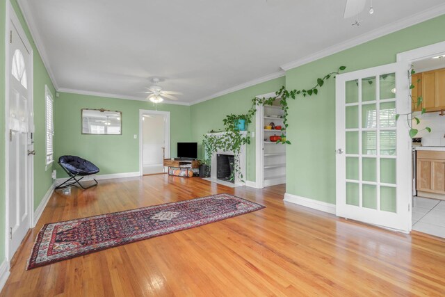 living room with a ceiling fan, baseboards, ornamental molding, and light wood-type flooring