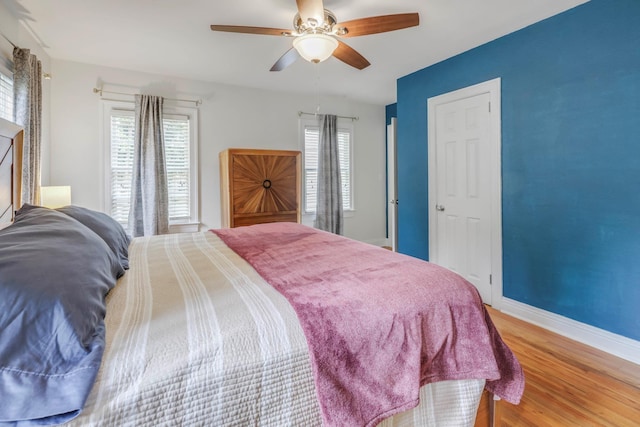 bedroom with baseboards, a ceiling fan, wood finished floors, and multiple windows