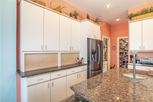 kitchen featuring stainless steel refrigerator with ice dispenser, white cabinetry, and dark stone countertops