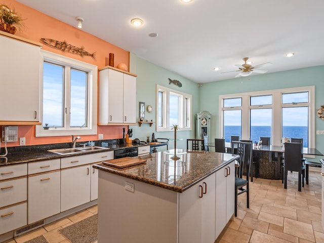 kitchen with a kitchen island, ceiling fan, sink, a water view, and white cabinetry