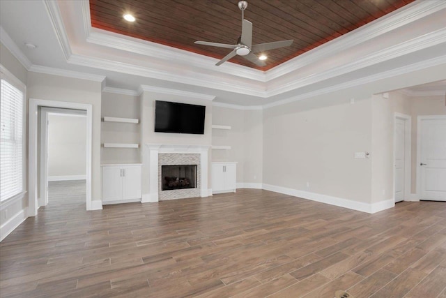 unfurnished living room featuring a raised ceiling, ceiling fan, built in features, and ornamental molding