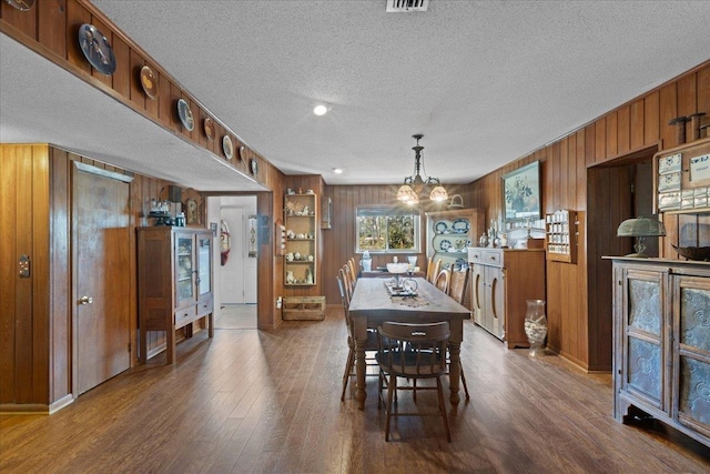 dining space with wood-type flooring, wooden walls, a textured ceiling, and a notable chandelier