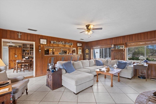 living room featuring light tile patterned flooring, ceiling fan, a textured ceiling, and wood walls