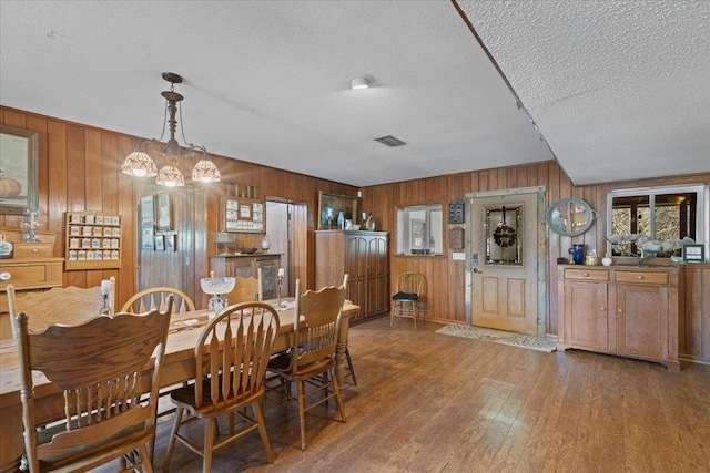 dining area with wooden walls, a chandelier, hardwood / wood-style floors, and a textured ceiling