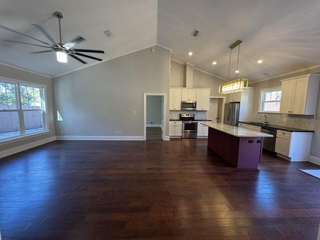 kitchen with appliances with stainless steel finishes, decorative light fixtures, a kitchen island, and crown molding