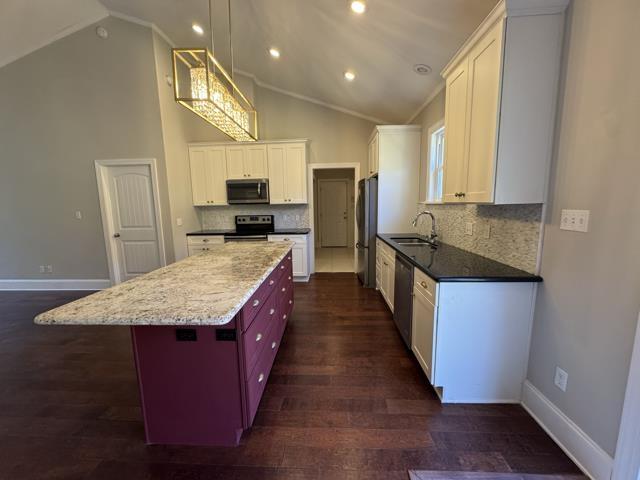 kitchen with decorative backsplash, appliances with stainless steel finishes, white cabinetry, and lofted ceiling