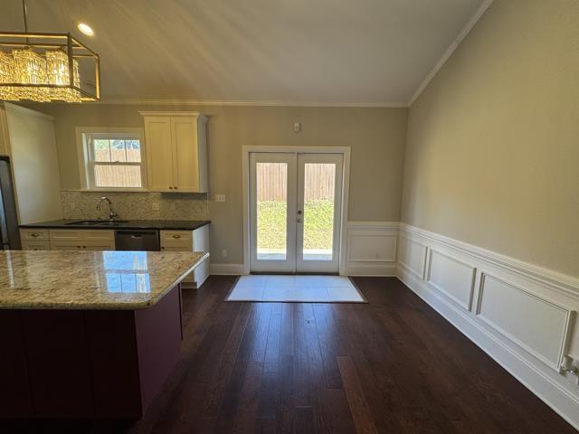 kitchen with light stone countertops, french doors, sink, pendant lighting, and ornamental molding