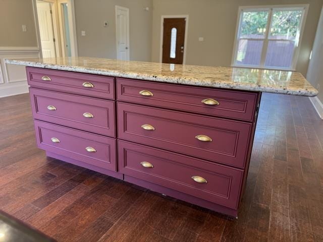 kitchen with a kitchen island, light stone counters, and dark wood-type flooring