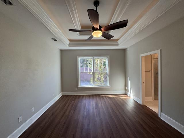 unfurnished room with a raised ceiling, ceiling fan, dark hardwood / wood-style flooring, and ornamental molding