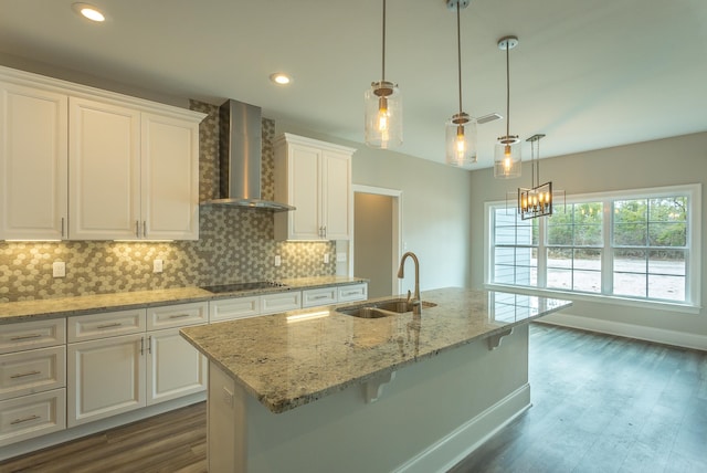 kitchen featuring wall chimney range hood, a kitchen island with sink, white cabinets, and a sink