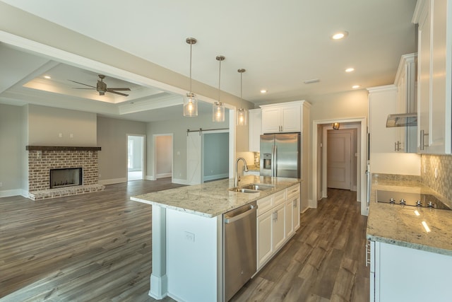 kitchen with decorative light fixtures, a barn door, appliances with stainless steel finishes, white cabinetry, and an island with sink