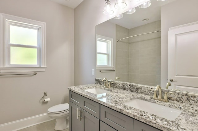 bathroom featuring toilet, double vanity, baseboards, and a sink