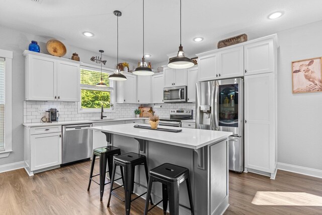 kitchen featuring white cabinetry, appliances with stainless steel finishes, decorative light fixtures, wood-type flooring, and a center island