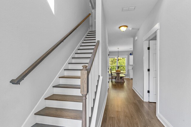 stairs featuring hardwood / wood-style flooring and an inviting chandelier