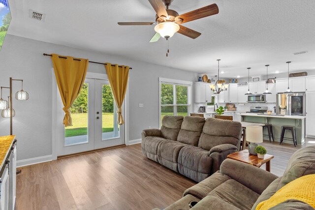 living room featuring a textured ceiling, light wood-type flooring, sink, and ceiling fan with notable chandelier