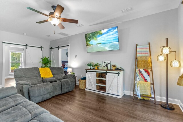 living room with a barn door, ceiling fan, and dark hardwood / wood-style floors