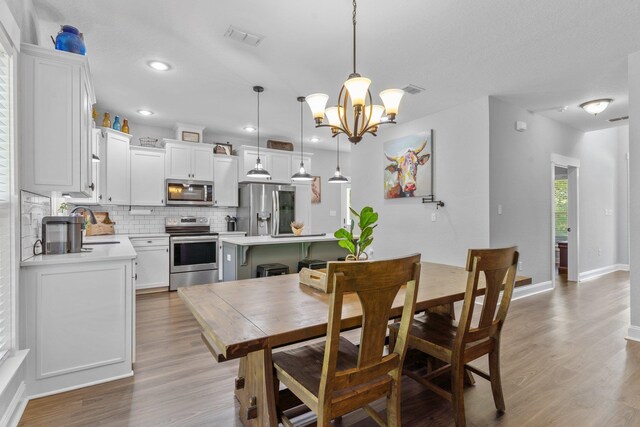 dining room with sink, light wood-type flooring, and an inviting chandelier