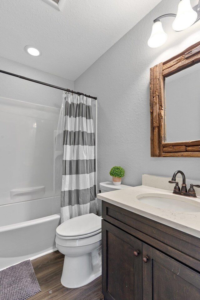 full bathroom featuring vanity, a textured ceiling, hardwood / wood-style floors, toilet, and shower / bath combo with shower curtain