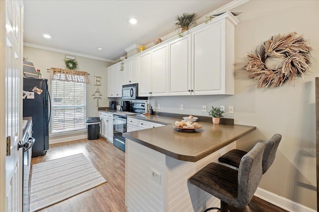 kitchen with white cabinetry, black appliances, a kitchen bar, kitchen peninsula, and light wood-type flooring