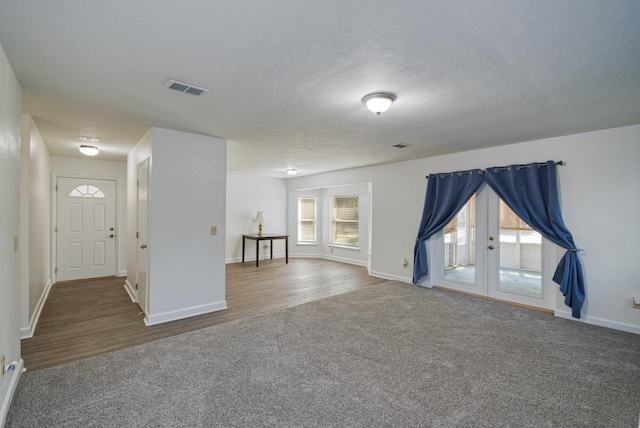 interior space featuring french doors, visible vents, a textured ceiling, wood finished floors, and baseboards